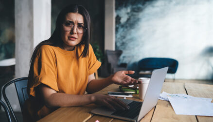 Confused young lady sitting at table with laptop